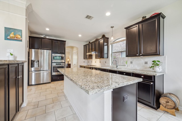 kitchen with appliances with stainless steel finishes, backsplash, light tile patterned floors, and a center island