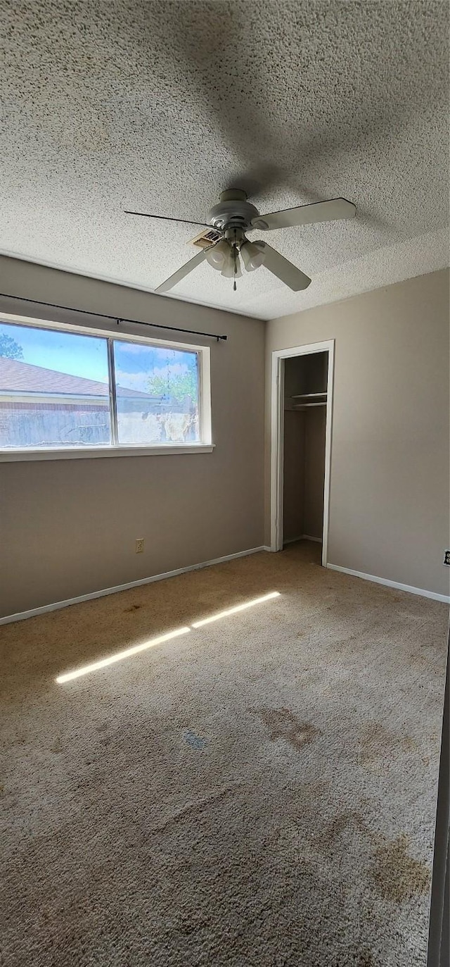 unfurnished bedroom with baseboards, ceiling fan, a textured ceiling, carpet flooring, and a closet