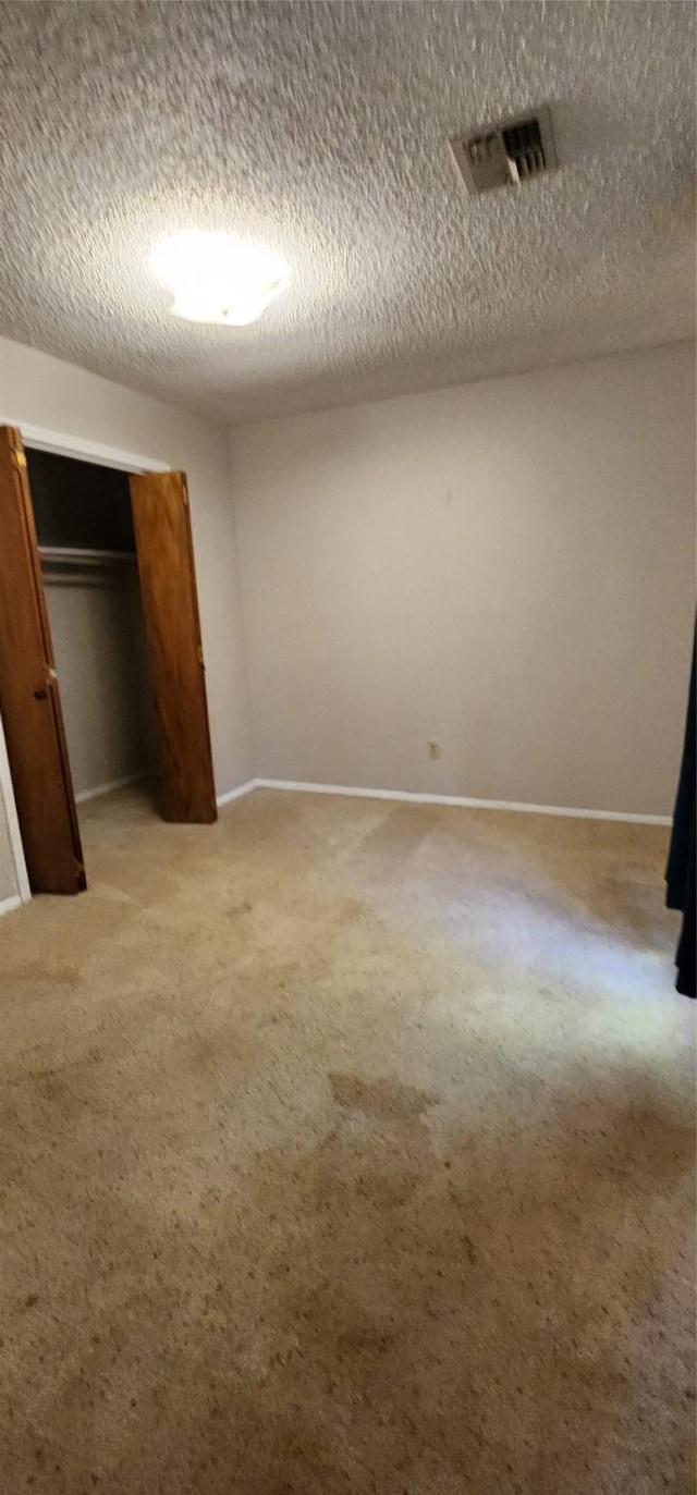 unfurnished bedroom featuring a textured ceiling, baseboards, visible vents, and light colored carpet