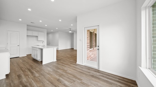 kitchen with ceiling fan, sink, hardwood / wood-style flooring, white cabinets, and an island with sink