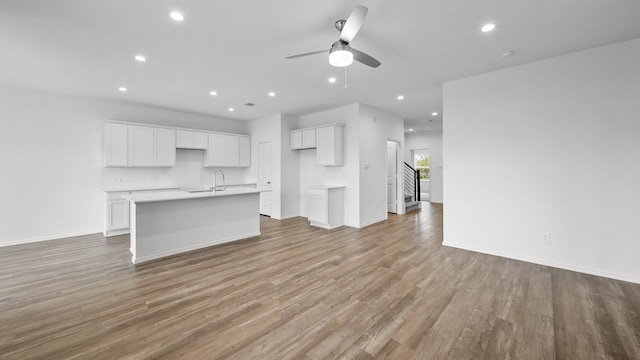 kitchen with light wood-type flooring, ceiling fan, sink, white cabinetry, and an island with sink