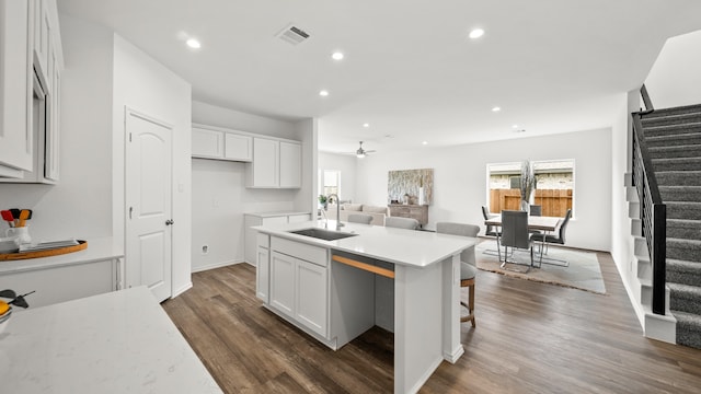 kitchen featuring dark wood-type flooring, white cabinets, sink, ceiling fan, and an island with sink