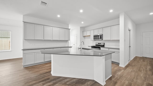 kitchen featuring dark hardwood / wood-style flooring, appliances with stainless steel finishes, sink, and an island with sink