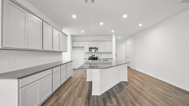 kitchen featuring wood-type flooring, white cabinetry, appliances with stainless steel finishes, sink, and a kitchen island with sink