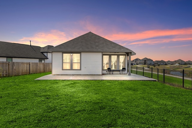 back house at dusk featuring a yard and a patio