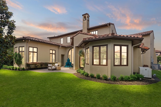 back house at dusk with central AC unit, an outdoor living space, a patio area, and a yard