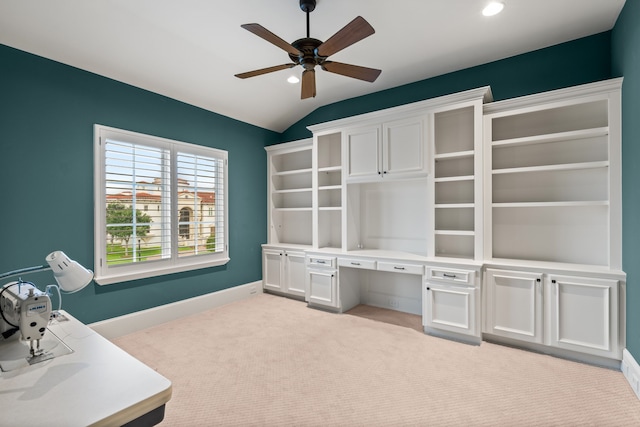 unfurnished office featuring lofted ceiling, built in desk, ceiling fan, and light carpet