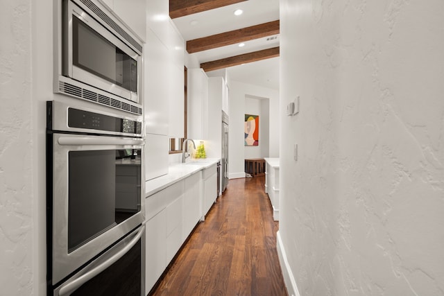 kitchen featuring stainless steel appliances, sink, dark wood-type flooring, beam ceiling, and white cabinets