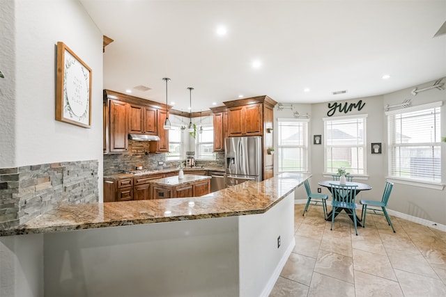 kitchen with decorative light fixtures, light stone countertops, backsplash, appliances with stainless steel finishes, and kitchen peninsula