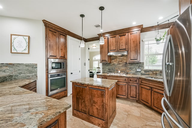 kitchen featuring tasteful backsplash, decorative light fixtures, a kitchen island, light stone countertops, and appliances with stainless steel finishes