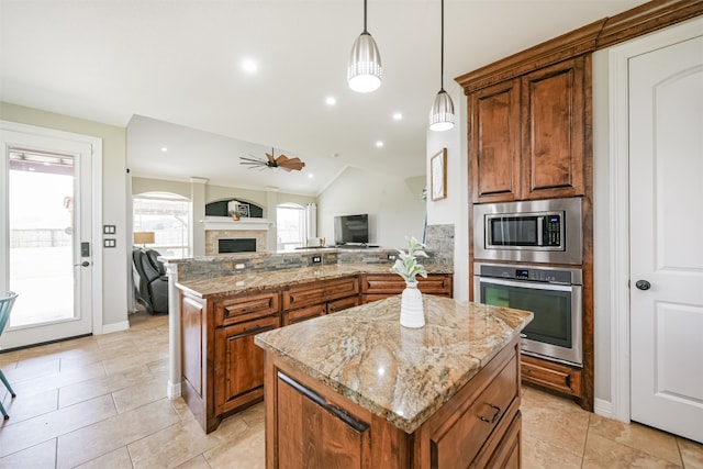 kitchen featuring a center island, vaulted ceiling, light stone countertops, stainless steel appliances, and pendant lighting