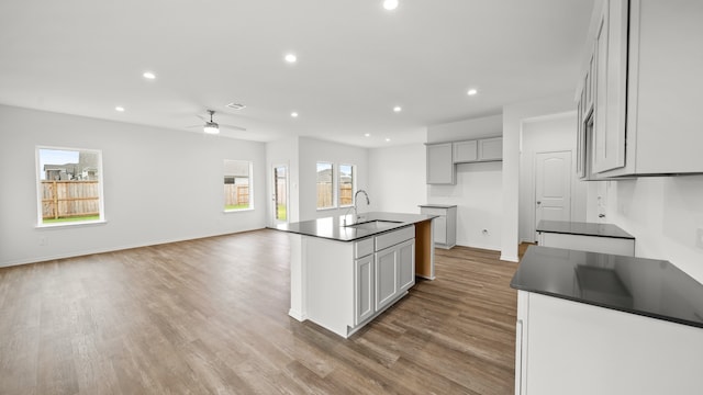 kitchen with ceiling fan, light hardwood / wood-style flooring, a kitchen island with sink, and sink