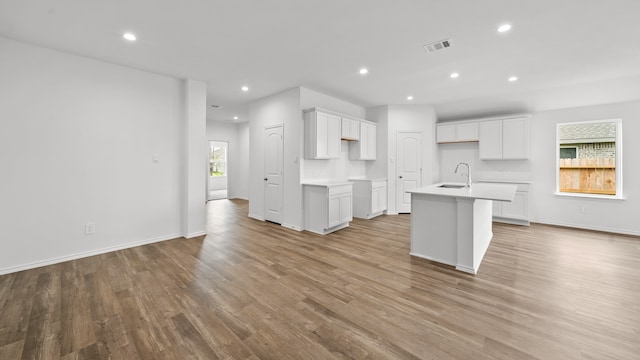 kitchen with white cabinets, light hardwood / wood-style floors, sink, and an island with sink