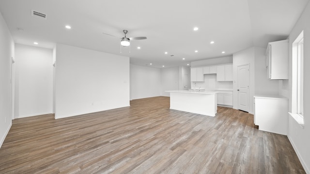 kitchen featuring ceiling fan, sink, a center island with sink, white cabinets, and light wood-type flooring