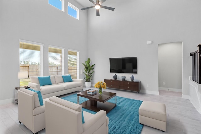 living room with ceiling fan, a healthy amount of sunlight, light wood-type flooring, and a high ceiling