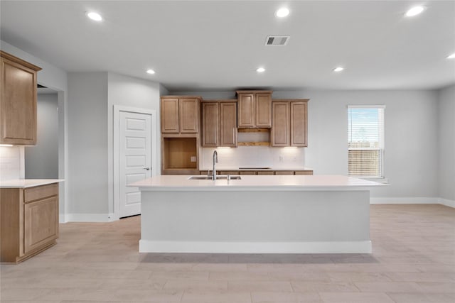 kitchen with backsplash, a center island with sink, light hardwood / wood-style floors, and sink