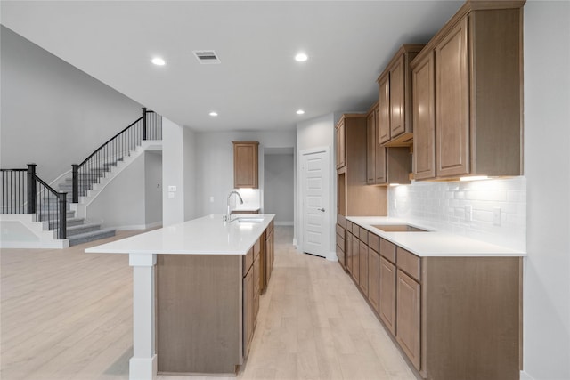 kitchen featuring sink, tasteful backsplash, light hardwood / wood-style flooring, and an island with sink