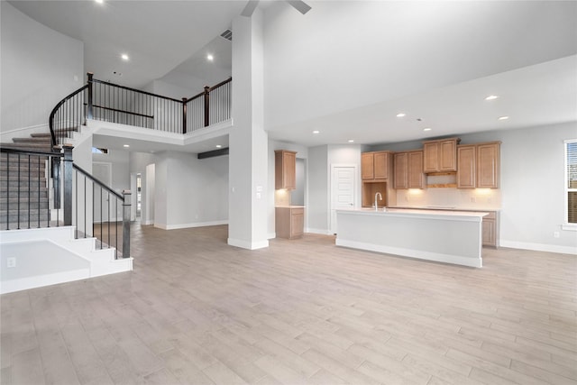 unfurnished living room featuring light hardwood / wood-style floors, a towering ceiling, and sink