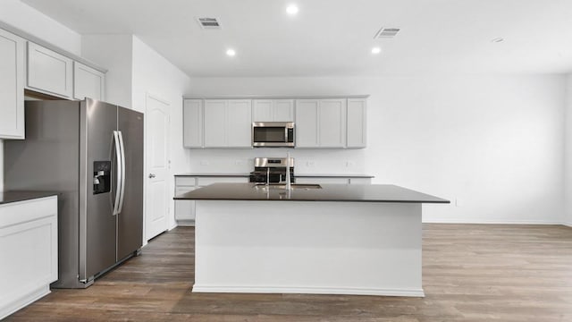 kitchen featuring wood-type flooring, appliances with stainless steel finishes, a kitchen island with sink, and sink