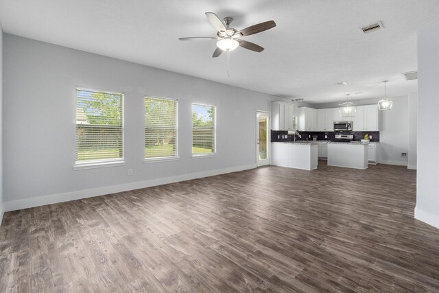 unfurnished living room with ceiling fan with notable chandelier and dark hardwood / wood-style floors