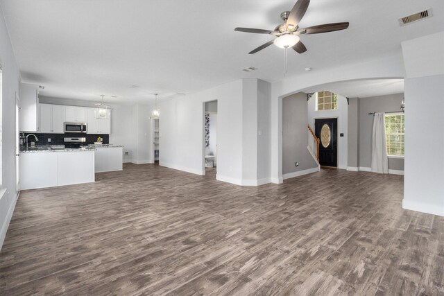 unfurnished living room featuring ceiling fan with notable chandelier and dark hardwood / wood-style flooring