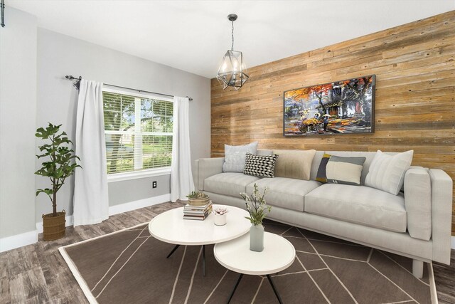 living room with dark hardwood / wood-style floors, wood walls, and an inviting chandelier