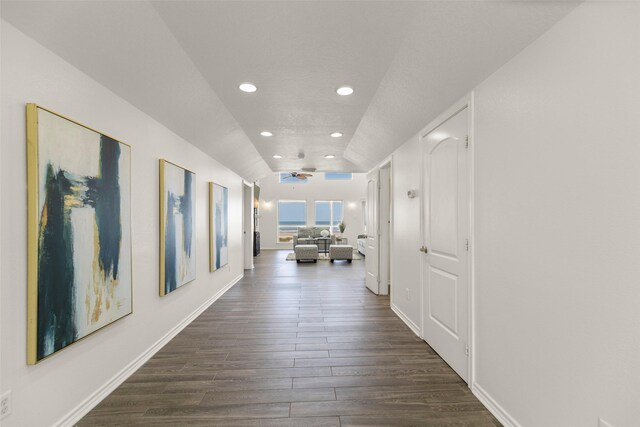 hall with dark wood-type flooring, vaulted ceiling, and a textured ceiling