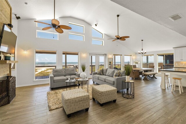 living room featuring high vaulted ceiling, a healthy amount of sunlight, light wood-type flooring, and ceiling fan with notable chandelier