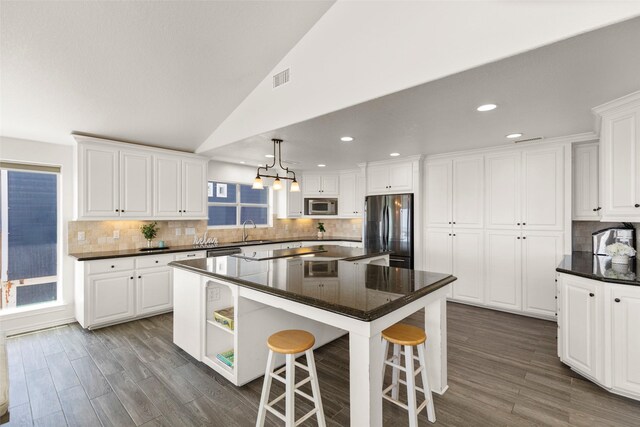 kitchen with a center island, a kitchen breakfast bar, stainless steel appliances, lofted ceiling, and white cabinets