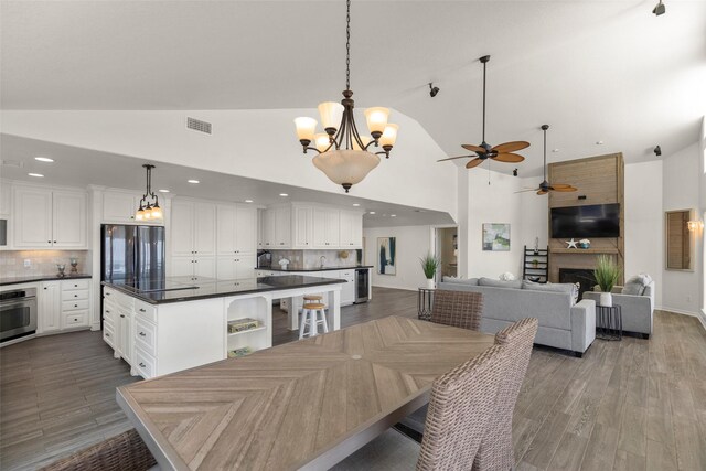 dining room with ceiling fan with notable chandelier, high vaulted ceiling, and dark hardwood / wood-style flooring