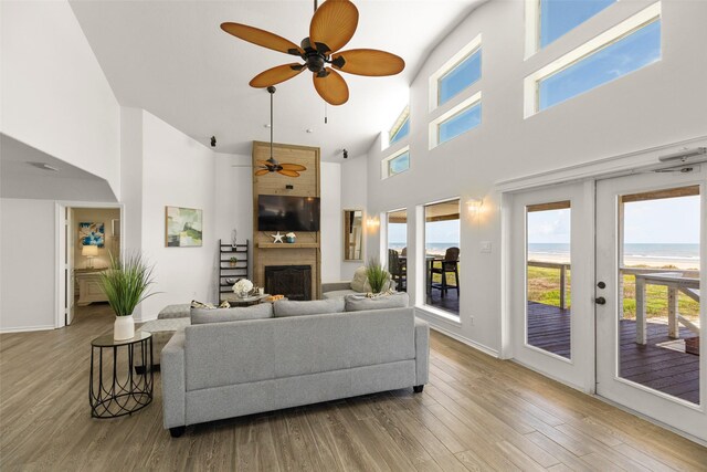 living room with a large fireplace, ceiling fan, light hardwood / wood-style flooring, a high ceiling, and french doors