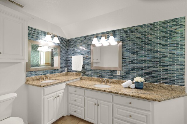 bathroom with lofted ceiling, vanity, decorative backsplash, and toilet