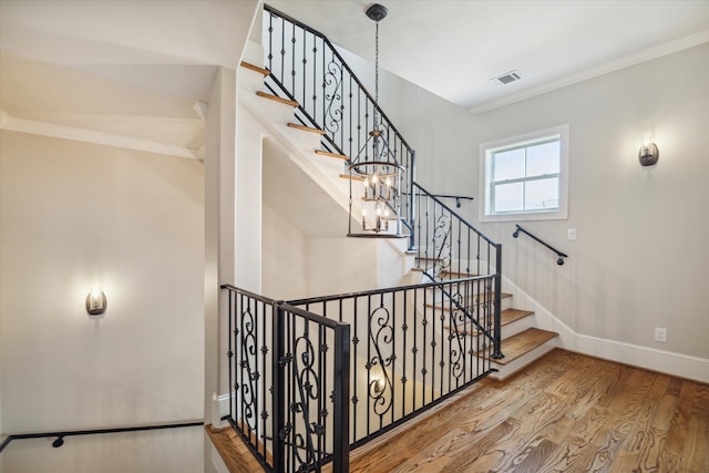 stairway featuring crown molding, hardwood / wood-style floors, and an inviting chandelier