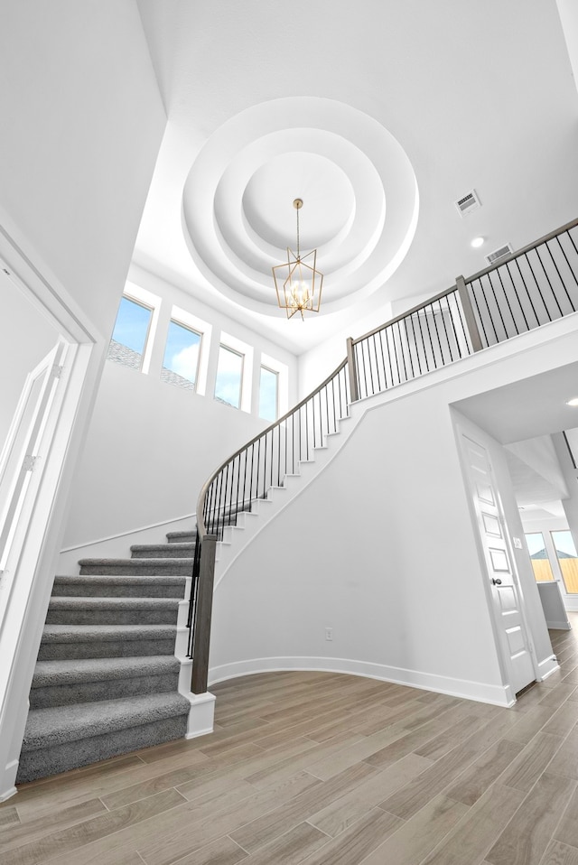 stairway with a notable chandelier, a towering ceiling, a wealth of natural light, and a tray ceiling