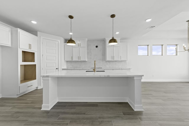 kitchen featuring pendant lighting, white cabinets, sink, an island with sink, and light stone counters