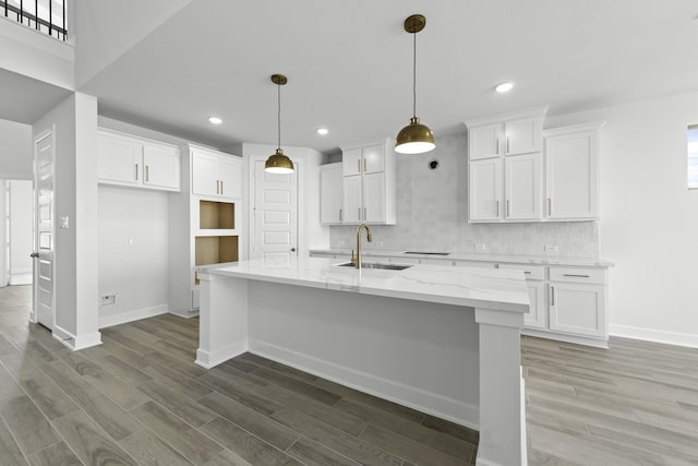 kitchen with white cabinets, sink, hanging light fixtures, light stone countertops, and an island with sink