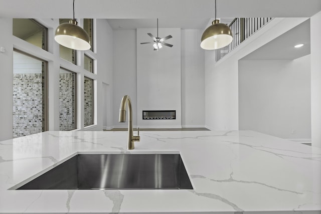 kitchen featuring light stone countertops, pendant lighting, ceiling fan, and sink