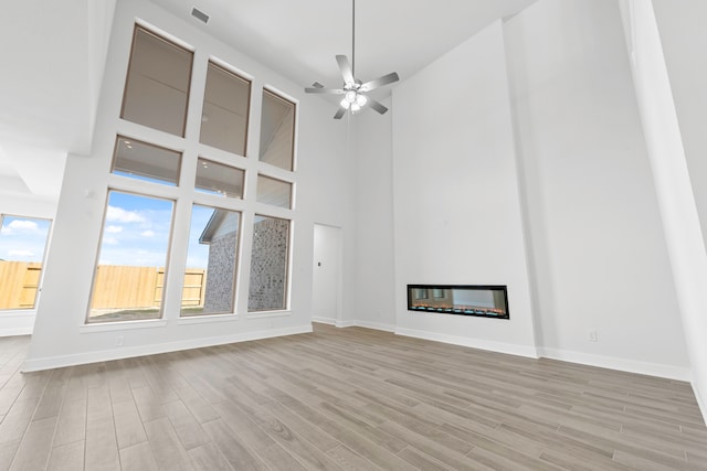 unfurnished living room with a towering ceiling, light hardwood / wood-style floors, and ceiling fan