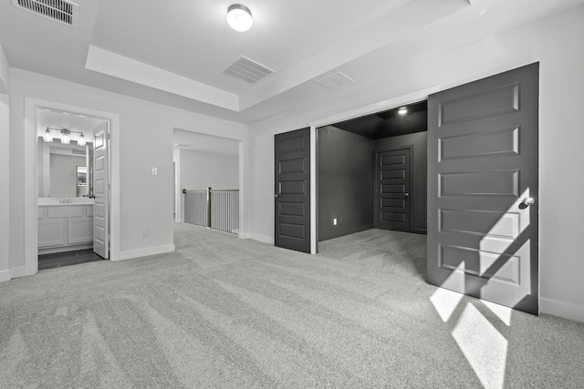 carpeted bedroom featuring ensuite bathroom, sink, and a tray ceiling