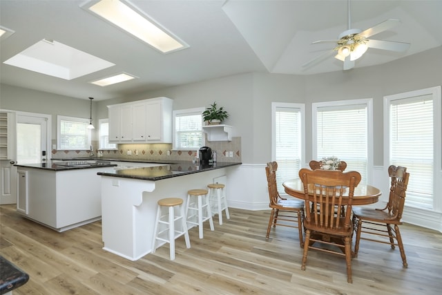 kitchen with hanging light fixtures, backsplash, white cabinetry, light hardwood / wood-style floors, and kitchen peninsula