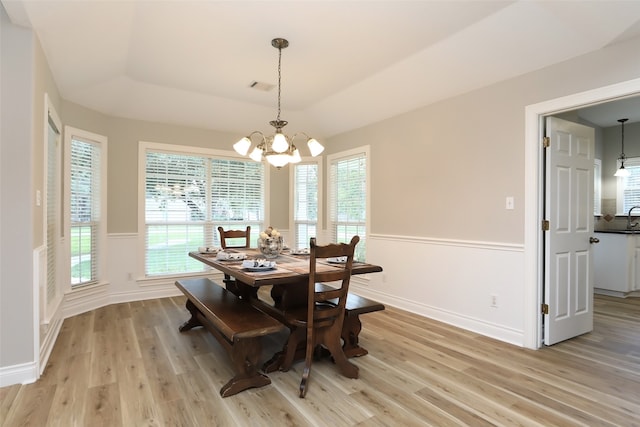 dining area with a notable chandelier, light wood-type flooring, and a tray ceiling