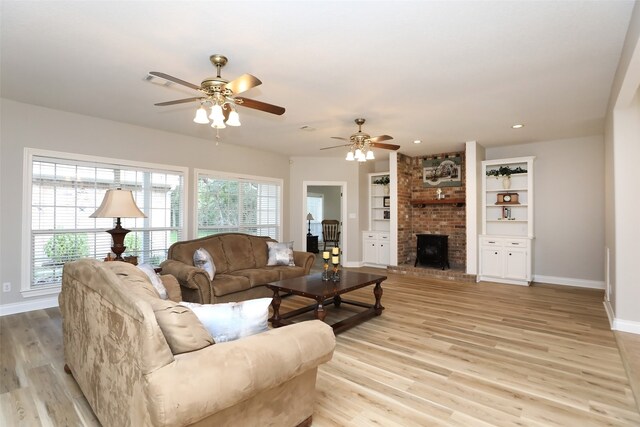 living room featuring brick wall, a fireplace, ceiling fan, and light hardwood / wood-style floors