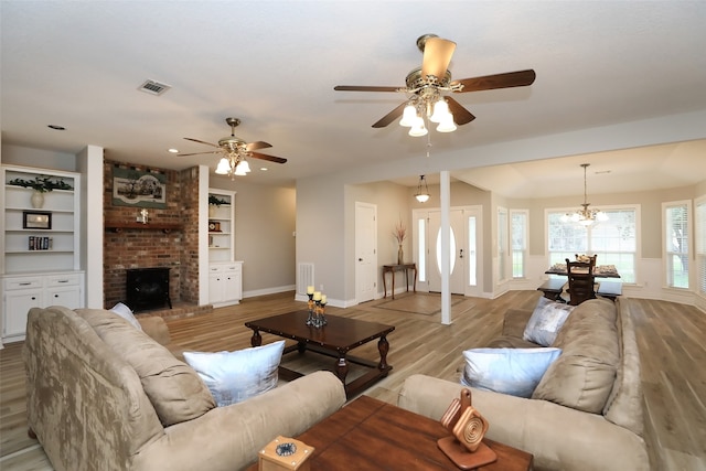 living room featuring brick wall, light hardwood / wood-style flooring, ceiling fan with notable chandelier, and a brick fireplace