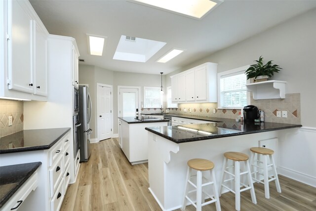 kitchen featuring tasteful backsplash, a kitchen breakfast bar, pendant lighting, light hardwood / wood-style floors, and a skylight