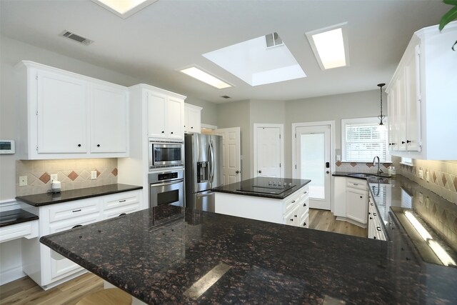 kitchen featuring appliances with stainless steel finishes, a skylight, white cabinets, and decorative light fixtures