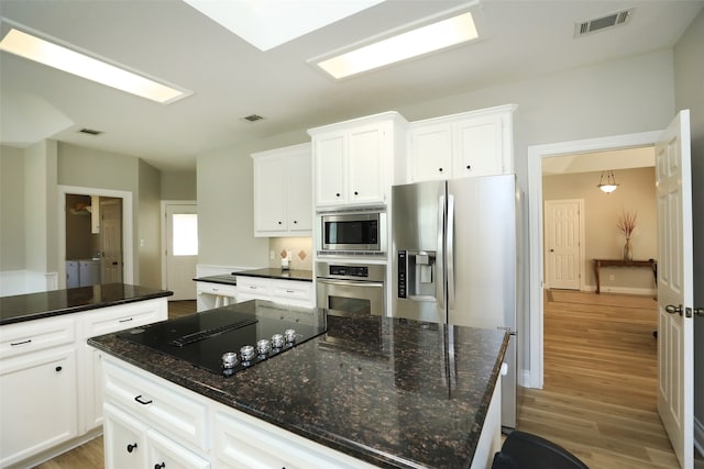 kitchen featuring light wood-type flooring, appliances with stainless steel finishes, a kitchen island, and dark stone counters