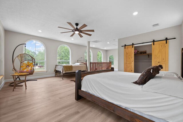 bedroom with ceiling fan, light wood-type flooring, a barn door, and multiple windows