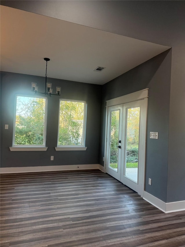 unfurnished dining area with french doors, a notable chandelier, dark hardwood / wood-style flooring, and a wealth of natural light