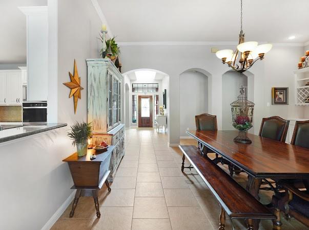 hall featuring crown molding, light tile patterned floors, and a notable chandelier