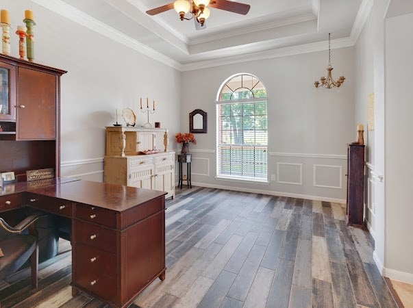 office space with ceiling fan with notable chandelier, a tray ceiling, ornamental molding, and hardwood / wood-style flooring